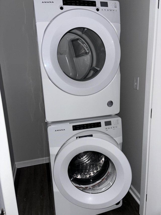 laundry area with stacked washer and dryer, wood finished floors, laundry area, and baseboards