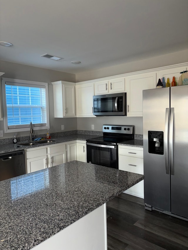 kitchen featuring dark wood-style floors, stainless steel appliances, visible vents, white cabinetry, and a sink