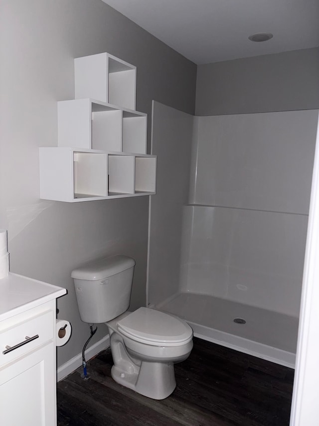 bathroom with baseboards, toilet, wood finished floors, walk in shower, and vanity