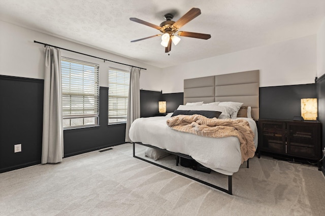 bedroom featuring a ceiling fan, visible vents, light carpet, and a textured ceiling