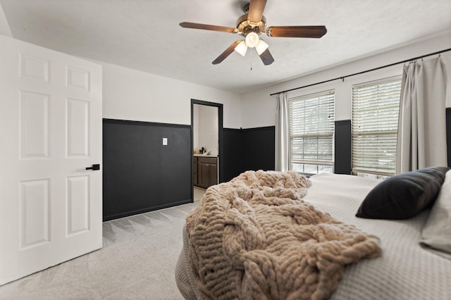 bedroom with a wainscoted wall, light colored carpet, ceiling fan, and a textured ceiling