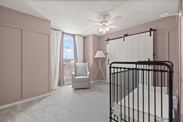 bedroom with carpet floors, a decorative wall, a barn door, a textured ceiling, and a nursery area