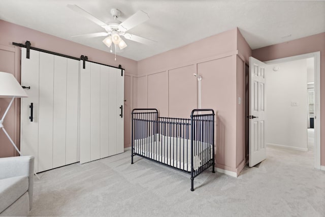 bedroom with light carpet, a barn door, a nursery area, and a ceiling fan