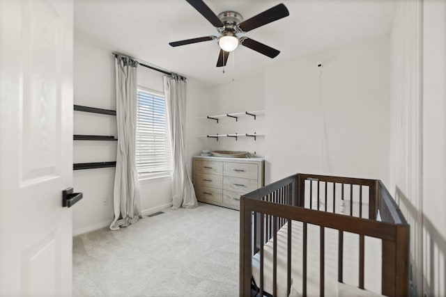 bedroom featuring visible vents, a ceiling fan, carpet flooring, a crib, and baseboards