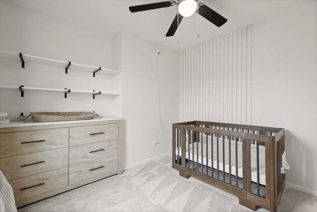 bedroom featuring light carpet, ceiling fan, a crib, and baseboards