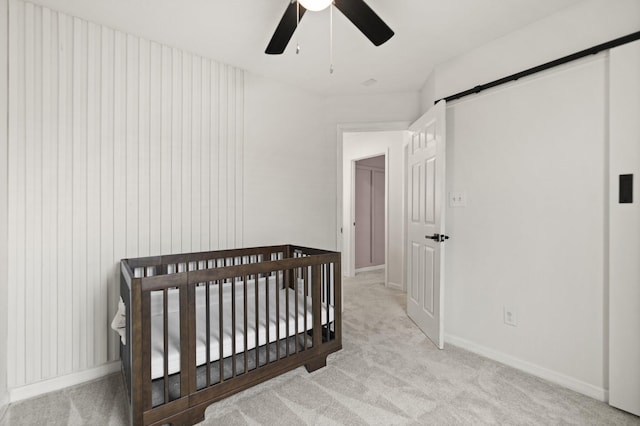 bedroom featuring ceiling fan, a barn door, light carpet, baseboards, and a crib