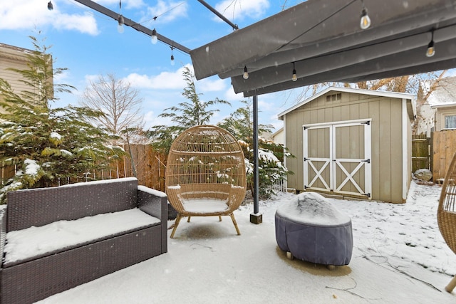 snow covered patio featuring outdoor lounge area, a shed, an outdoor structure, and fence