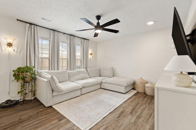 living room with a ceiling fan, light wood-style flooring, visible vents, and a textured ceiling