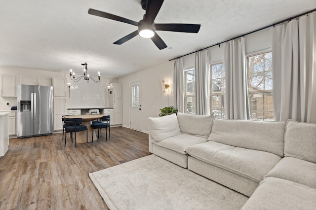 living area with a textured ceiling, ceiling fan with notable chandelier, and light wood-style flooring