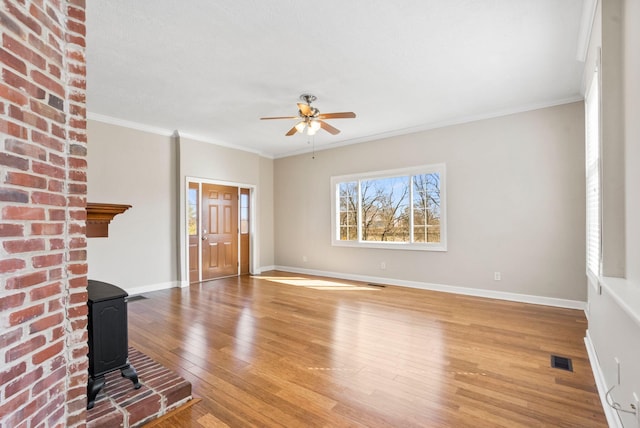 unfurnished living room featuring visible vents, light wood-style flooring, ornamental molding, a wood stove, and baseboards