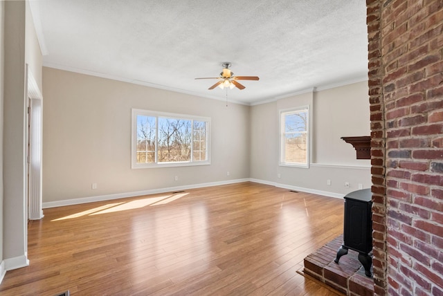 unfurnished living room featuring a textured ceiling, light wood-style flooring, a wood stove, and crown molding