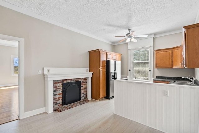 kitchen featuring light wood-style flooring, a brick fireplace, a sink, and stainless steel refrigerator with ice dispenser