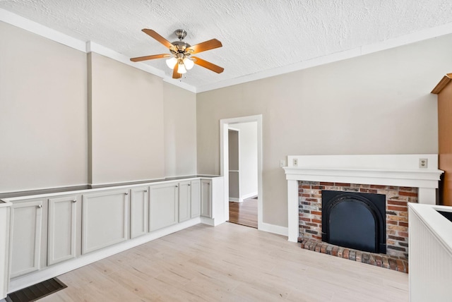 unfurnished living room featuring a textured ceiling, ceiling fan, visible vents, light wood-type flooring, and a brick fireplace