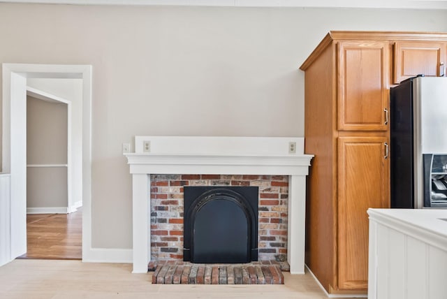 details featuring a brick fireplace, stainless steel refrigerator with ice dispenser, baseboards, and wood finished floors