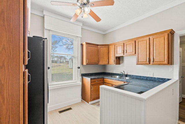 kitchen with visible vents, dark countertops, freestanding refrigerator, light wood-style floors, and a sink