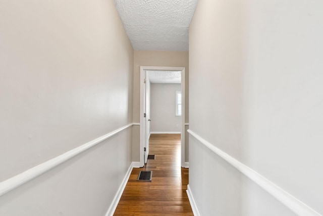 hall featuring visible vents, a textured ceiling, baseboards, and wood finished floors