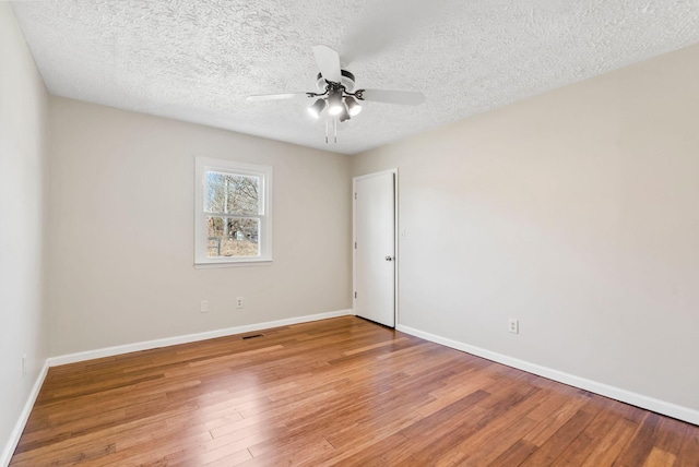 spare room featuring light wood-style floors, ceiling fan, baseboards, and a textured ceiling