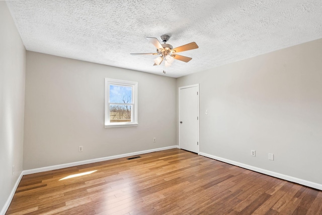 empty room with visible vents, ceiling fan, baseboards, and wood finished floors