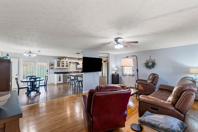 living area with ceiling fan with notable chandelier, a textured ceiling, and wood finished floors