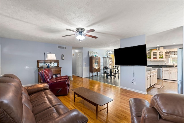 living area with a textured ceiling, visible vents, baseboards, a ceiling fan, and light wood finished floors