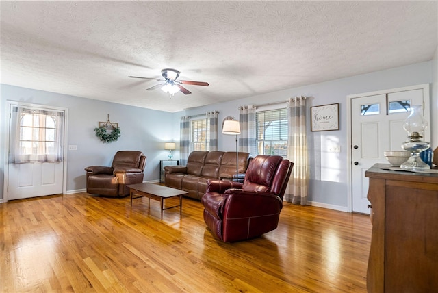 living area featuring baseboards, a textured ceiling, a ceiling fan, and light wood-style floors