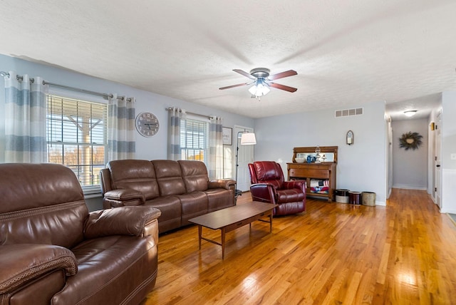 living area featuring light wood-style floors, visible vents, a textured ceiling, and a ceiling fan