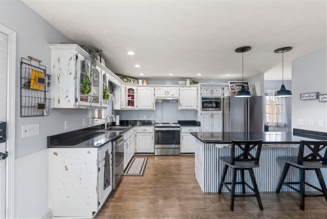 kitchen with dark countertops, dark wood-style floors, a breakfast bar, stainless steel appliances, and a sink