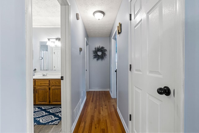 corridor with a sink, dark wood-style floors, baseboards, and a textured ceiling