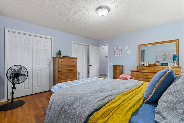 bedroom featuring a textured ceiling, visible vents, multiple closets, and wood finished floors