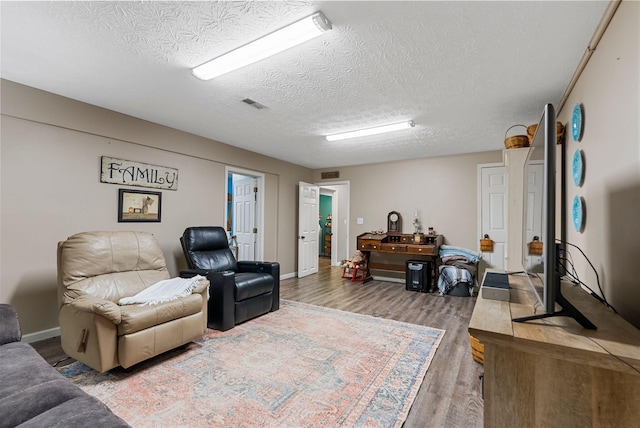 living area with visible vents, a textured ceiling, baseboards, and wood finished floors