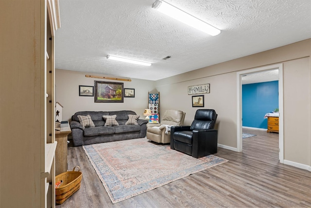 living area with a textured ceiling, wood finished floors, visible vents, and baseboards