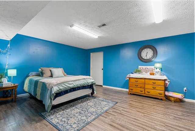 bedroom with a textured ceiling, wood finished floors, visible vents, and baseboards