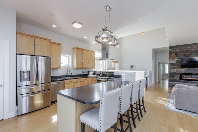 kitchen featuring appliances with stainless steel finishes, open floor plan, light brown cabinets, a sink, and island range hood