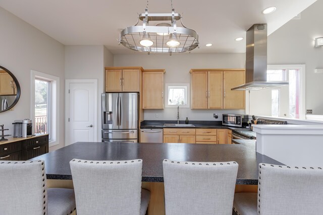 kitchen with dark countertops, island exhaust hood, stainless steel appliances, light brown cabinets, and a sink