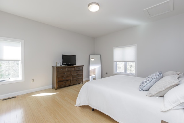 bedroom with light wood finished floors, attic access, visible vents, and baseboards