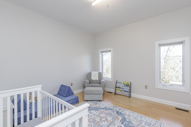 bedroom featuring a crib, baseboards, visible vents, and wood finished floors