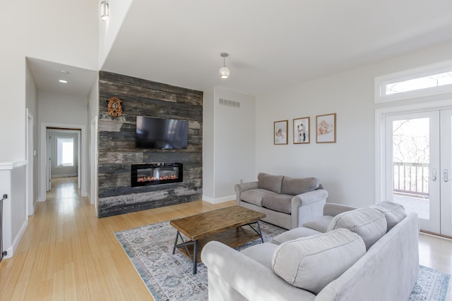 living room featuring a large fireplace, visible vents, baseboards, french doors, and light wood-type flooring