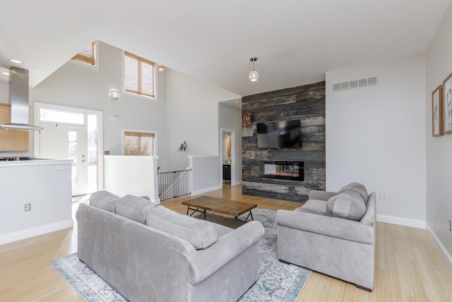 living area with a large fireplace, baseboards, visible vents, and wood finished floors