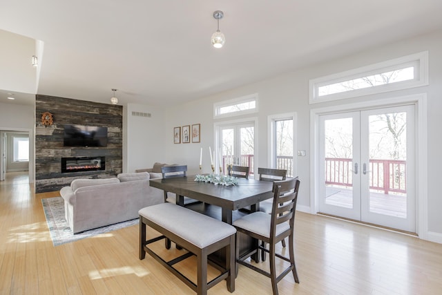 dining space featuring light wood-type flooring, a large fireplace, visible vents, and french doors