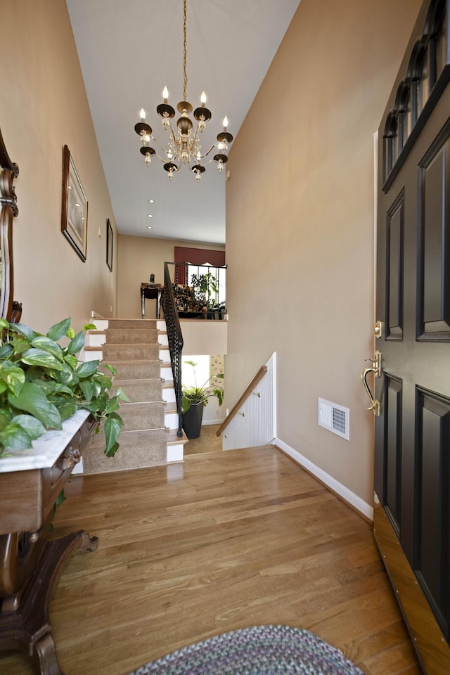 foyer entrance with a chandelier, wood finished floors, visible vents, baseboards, and stairway