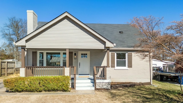 bungalow featuring covered porch, brick siding, and a chimney