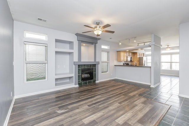 unfurnished living room with built in shelves, visible vents, a ceiling fan, a tile fireplace, and baseboards