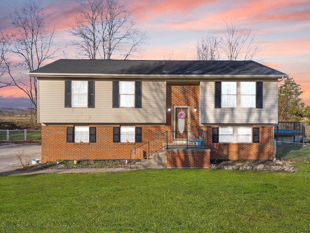 split foyer home featuring brick siding, a yard, and fence