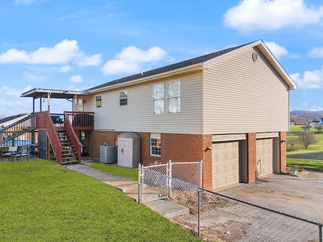 back of house with driveway, stairs, central air condition unit, a lawn, and brick siding