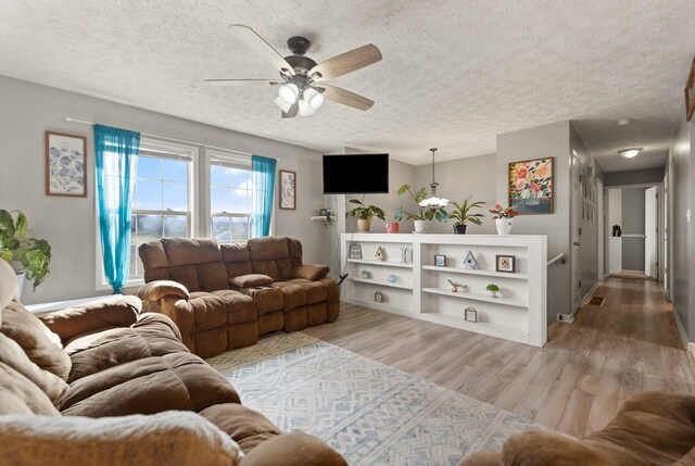 living room featuring light wood finished floors, visible vents, a textured ceiling, and a ceiling fan