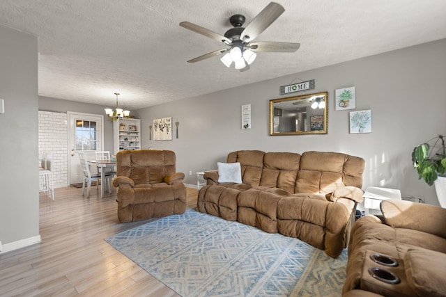 living room featuring baseboards, ceiling fan with notable chandelier, a textured ceiling, and light wood-style floors