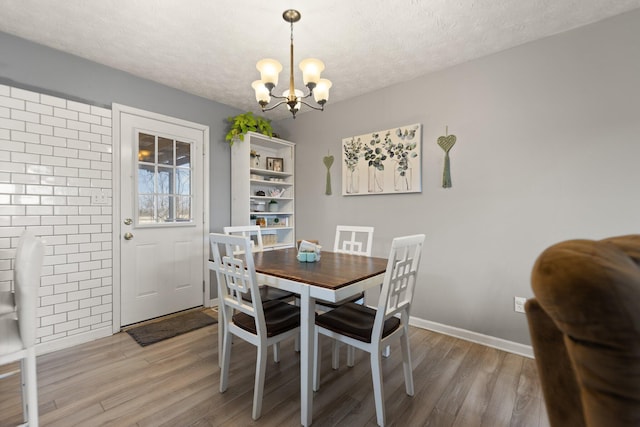 dining space with an inviting chandelier, light wood-style flooring, baseboards, and a textured ceiling