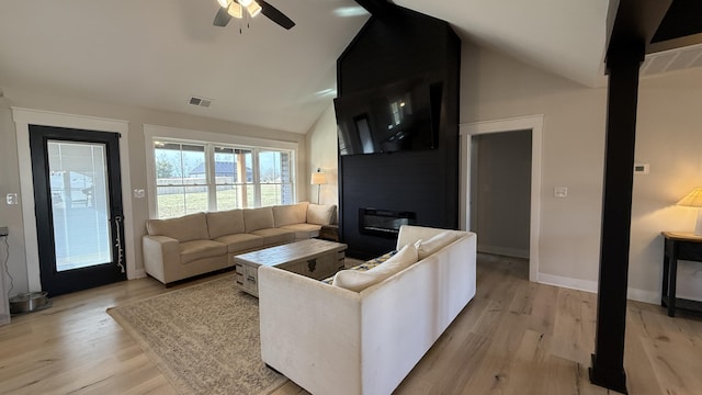 living room featuring lofted ceiling, light wood-type flooring, visible vents, and baseboards