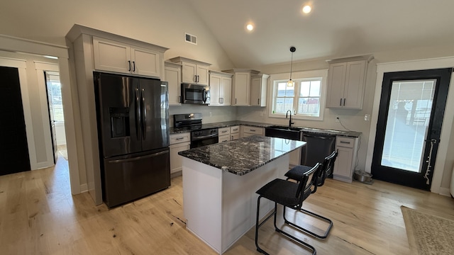 kitchen with a breakfast bar area, hanging light fixtures, a kitchen island, dark stone counters, and black appliances