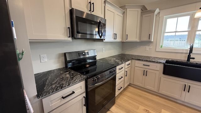 kitchen featuring light wood finished floors, stainless steel microwave, electric range, a sink, and dark stone counters